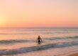 Swimmer entering the calm ocean at sunrise with soft colorful sky