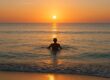 Solo swimmer at calm sunrise beach